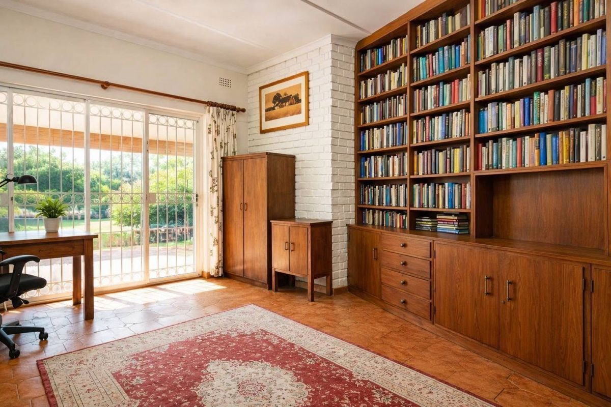 A bright living room featuring a large built-in wooden bookshelf, a painted brick fireplace, and sliding glass doors leading to the garden.