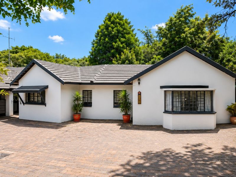 A well-maintained single-story home featuring a white facade, dark trim, a tiled roof, and a spacious brick-paved driveway.