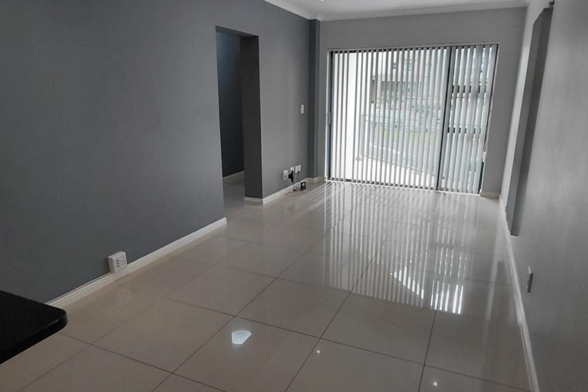 A bright, empty living area featuring polished tile flooring, neutral grey walls, and a large sliding glass door with vertical blinds leading outside.