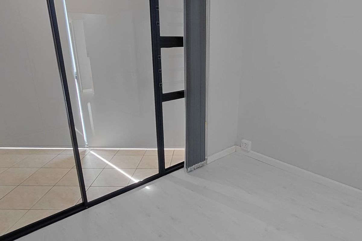 An empty bedroom featuring light-toned laminate flooring, neutral walls, and a sliding glass door providing access to an adjacent tiled balcony area.
