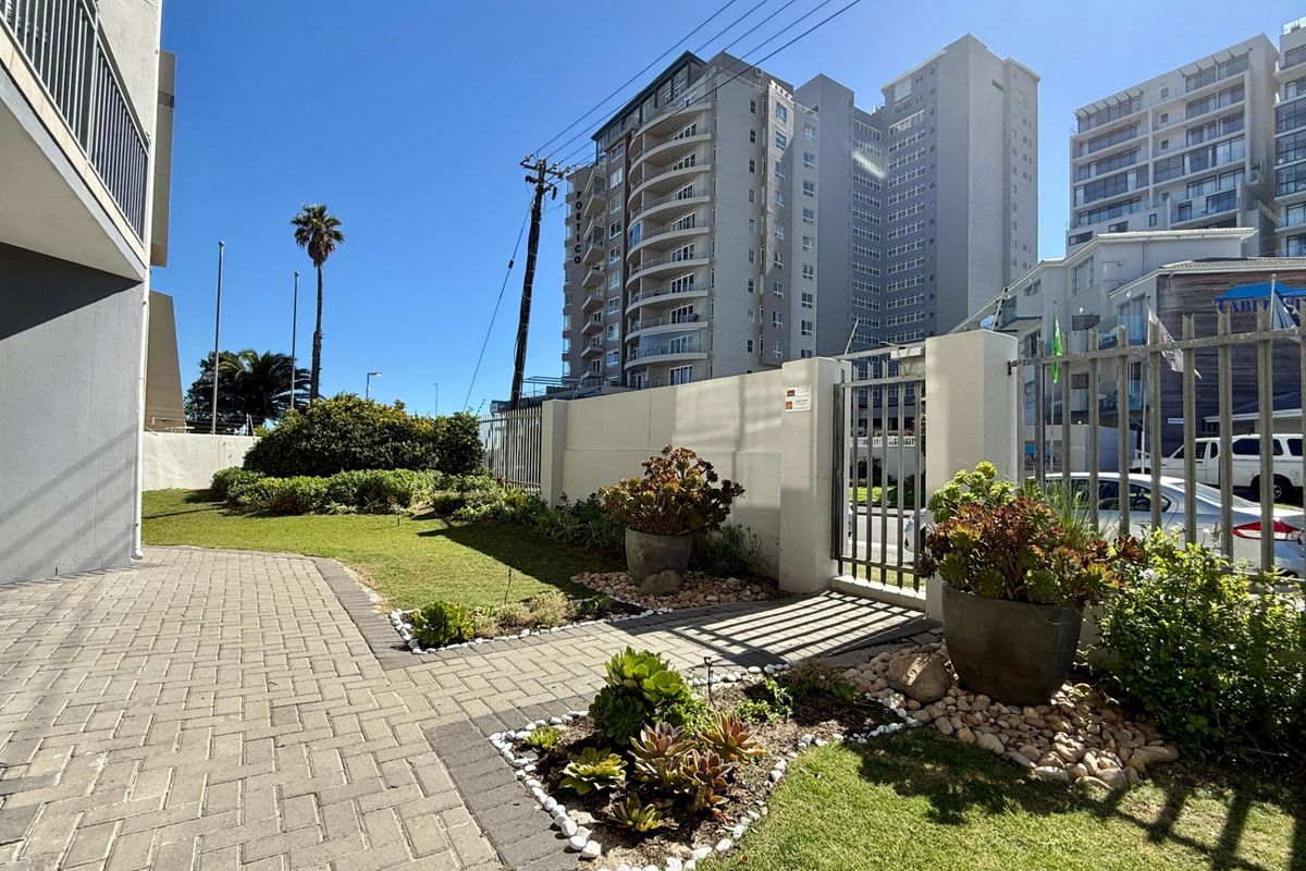 A well-maintained rear garden area featuring a paved walkway, landscaped garden beds, and a secure metal gate leading to the exterior perimeter.