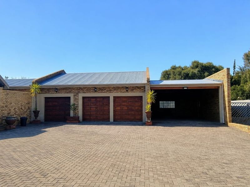 Spacious exterior view featuring a triple garage, an additional carport, and a large paved driveway with facebrick architectural detailing.