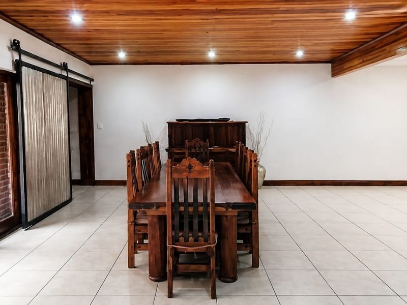 Spacious dining room featuring a warm timber-clad ceiling, recessed lighting, tiled floors, and an exposed brick feature wall with access to the patio.