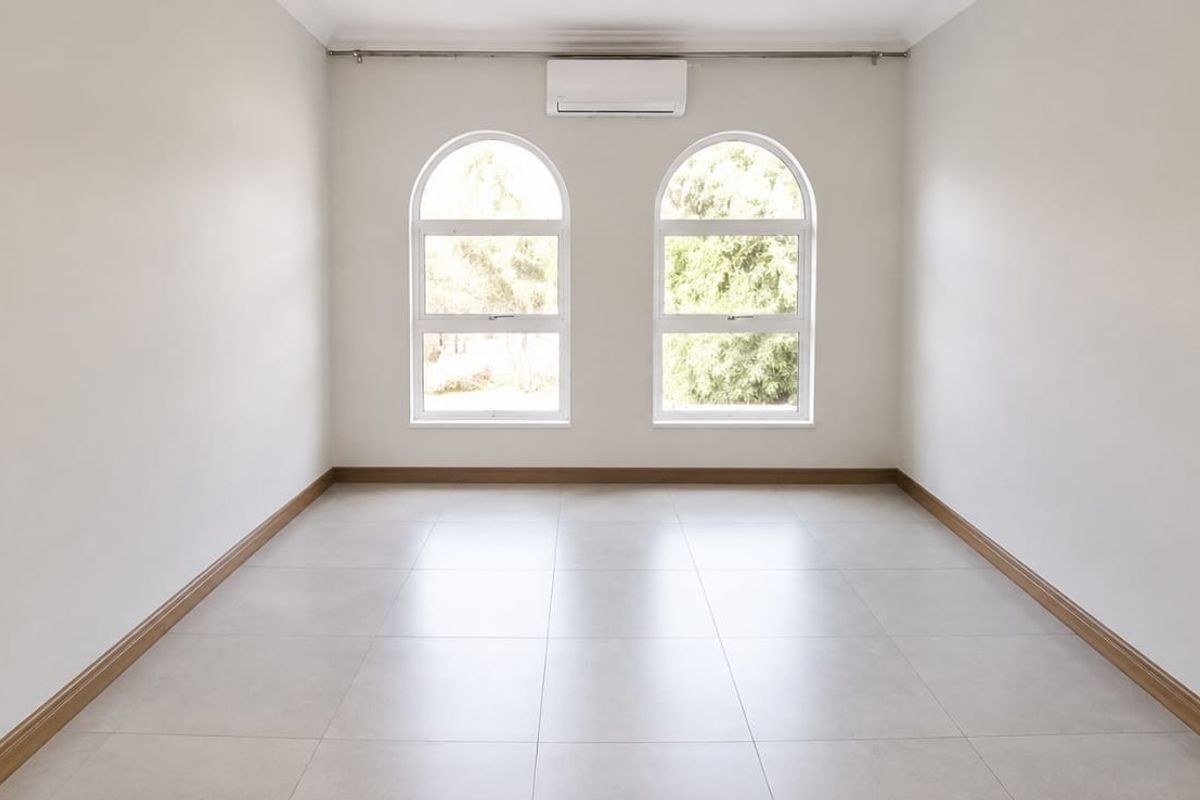 A bright, empty bedroom featuring neutral tiled flooring, arched windows, and a wall-mounted split-system air conditioning unit.