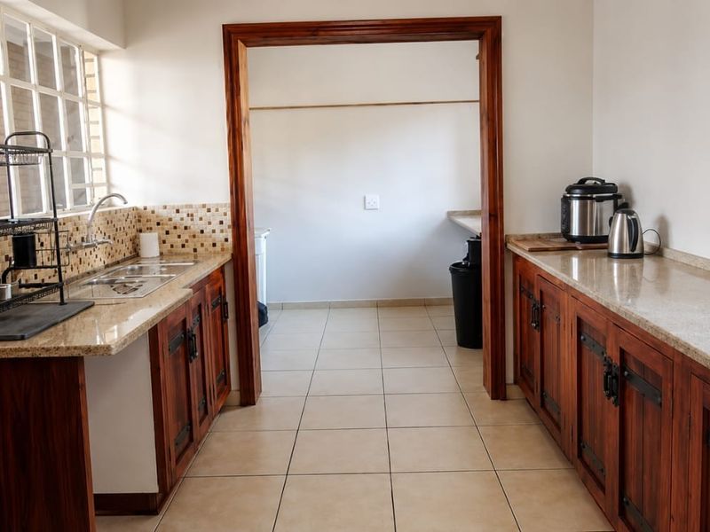 A functional scullery featuring wooden cabinetry, granite countertops, a stainless steel sink, and tiled flooring, providing ample prep and storage space.
