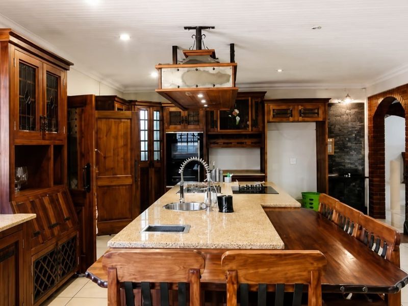Spacious kitchen featuring extensive wooden cabinetry, a large granite-topped island with integrated hob and sink, and a distinct rustic aesthetic.