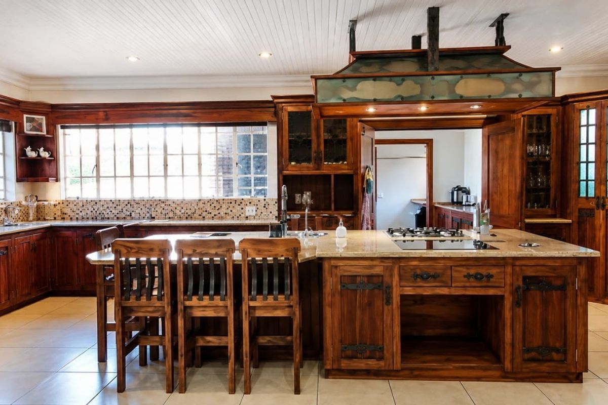 Spacious kitchen featuring extensive custom wooden cabinetry, a large central island with stone countertops, built-in appliances, and a decorative overhead extractor canopy.