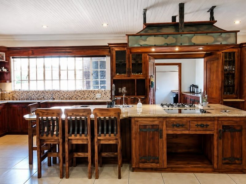 Spacious kitchen featuring extensive custom wooden cabinetry, a large central island with stone countertops, built-in appliances, and a decorative overhead extractor canopy.
