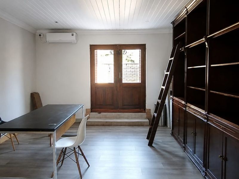 A spacious living area featuring a large built-in wooden library shelving unit with a ladder, tongue and groove ceiling, and direct access to the exterior.