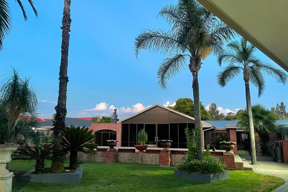 A view of the rear exterior featuring a brick facade, a paved patio area, and a well-maintained landscaped garden with mature palm trees.