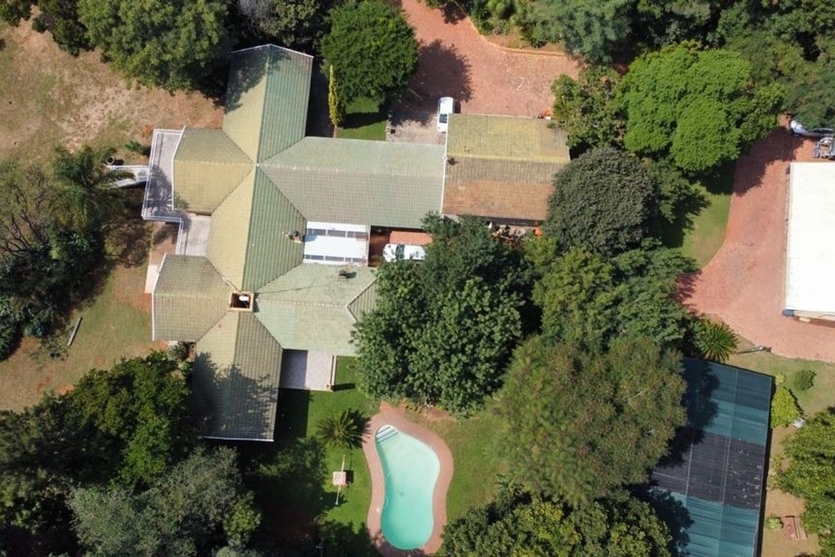 Aerial view of the property showcasing the main house with a tiled roof, swimming pool, expansive garden, and a separate outbuilding.