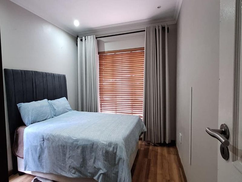 A well-maintained bedroom featuring warm wooden flooring, modern recessed downlights, and elegant window treatments with venetian blinds.