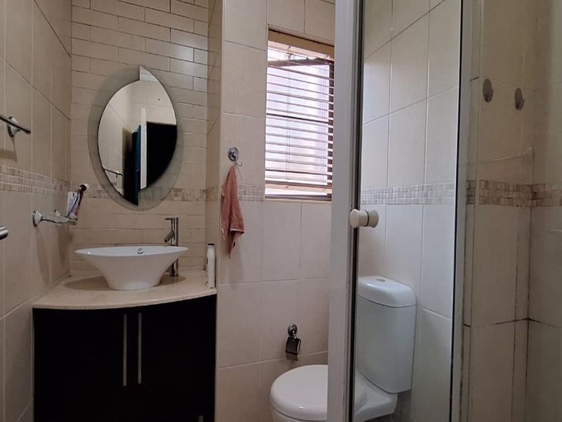 Compact bathroom featuring a vessel sink with vanity cabinet, a toilet, and a glass-enclosed shower with neutral wall tiling.