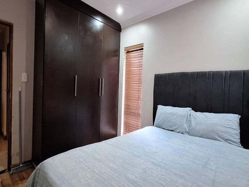 A well-maintained bedroom featuring dark wood built-in wardrobes, venetian blinds, and recessed ceiling lighting.