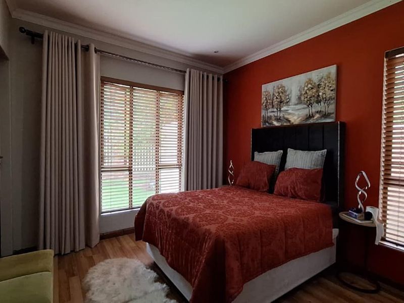 A well-maintained bedroom featuring warm-toned walls, wooden flooring, and large windows with fitted venetian blinds and curtain tracks.
