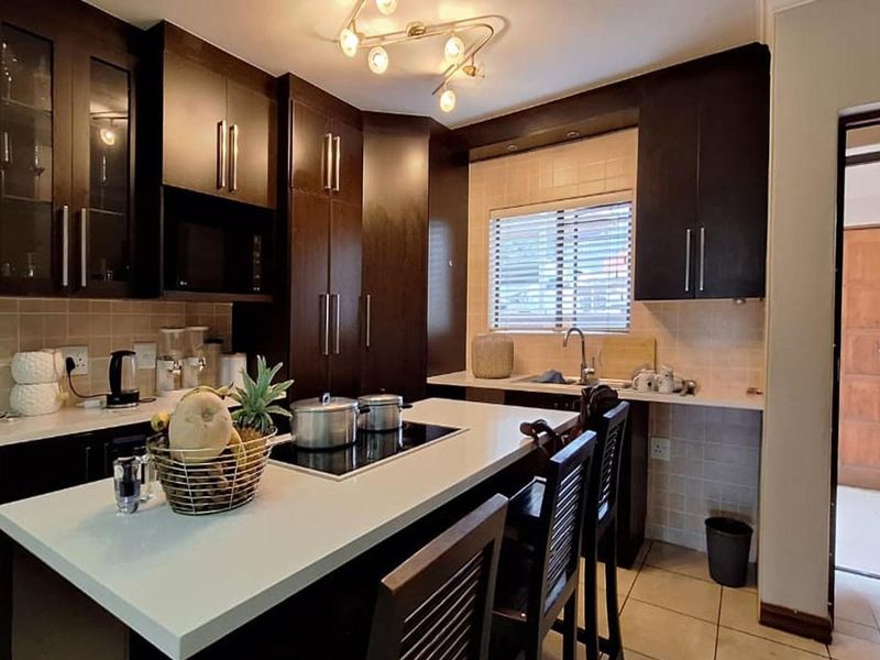 A well-maintained kitchen featuring dark wood cabinetry, stone countertops, a central island with a built-in hob, and tiled flooring.
