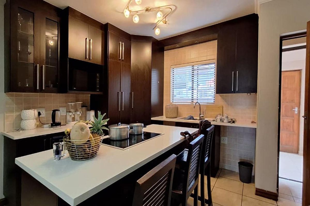 A well-maintained kitchen featuring dark wood cabinetry, stone countertops, a central island with a built-in hob, and tiled flooring.