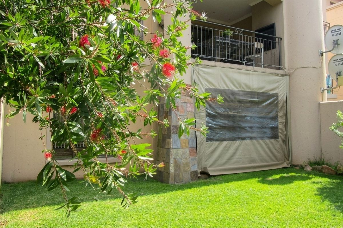 Rear view of the apartment featuring a private garden, a stone-clad pillar, and a covered balcony with a protective canvas enclosure.