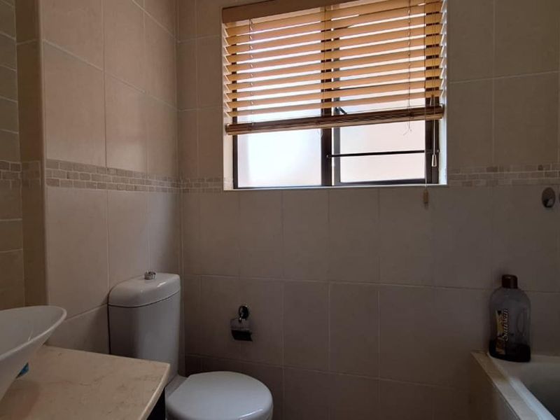 A functional bathroom featuring a vessel sink, toilet, and bathtub with neutral wall tiling and fitted venetian blinds.