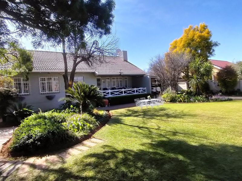 A well-maintained rear garden featuring a spacious lawn, mature landscaping, and a covered patio area attached to the main residence.