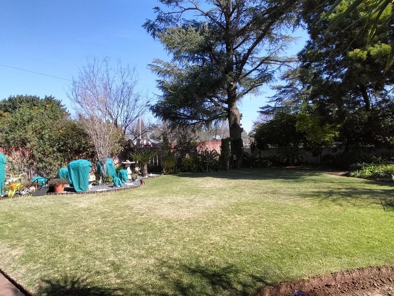 A spacious, well-maintained garden featuring a large lawn, mature trees, and brick boundary walling.