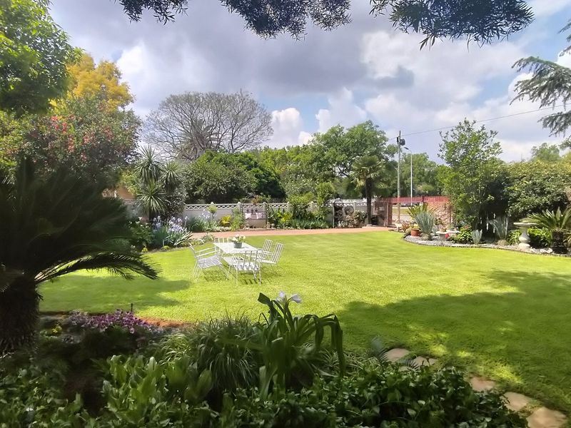 A well-maintained, spacious private garden featuring a lush green lawn, mature trees, and established perimeter walling.