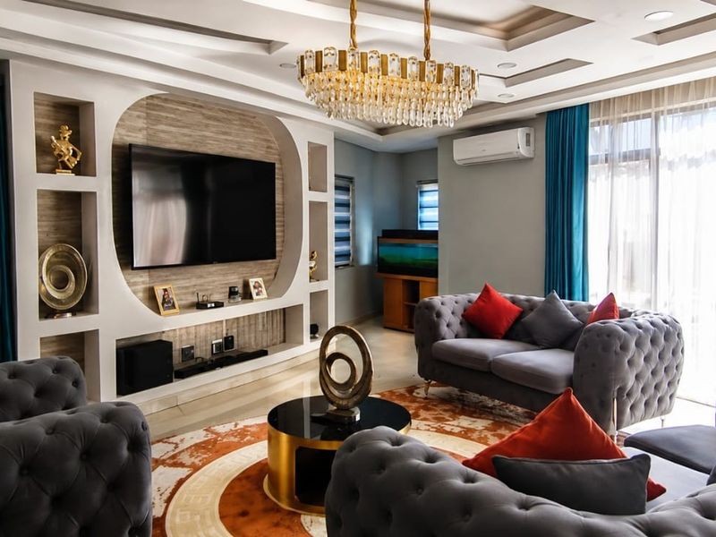 Spacious living room featuring a custom built-in media wall, elegant coffered ceiling with recessed lighting, and a sophisticated crystal chandelier.