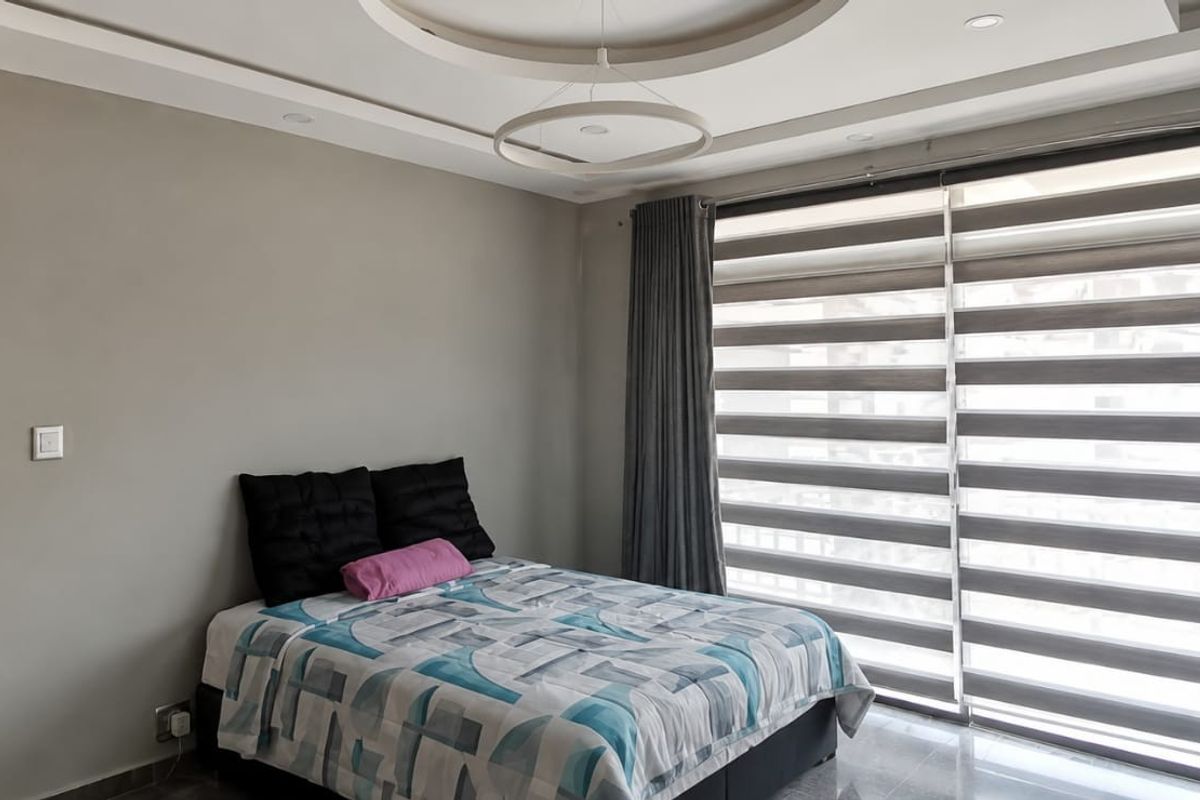 A well-maintained bedroom featuring a modern recessed ceiling design, tiled flooring, and large windows fitted with contemporary zebra blinds for adjustable natural light.