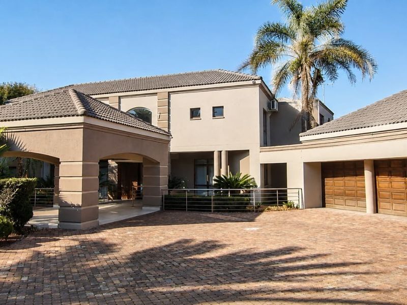 A well-maintained front elevation featuring a spacious paved driveway, a triple garage with wooden doors, and a grand covered entrance portico.