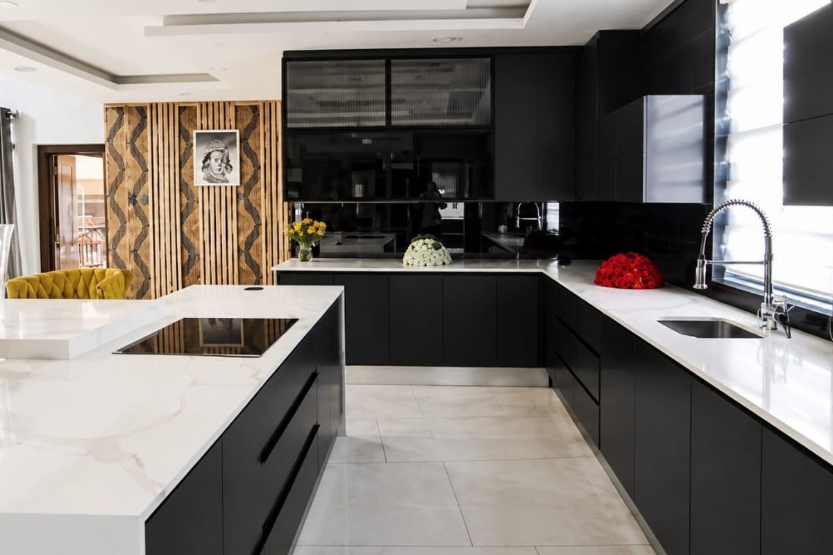 Modern kitchen featuring sleek black cabinetry, white stone countertops, a large central island with an integrated hob, and stylish decorative wall paneling.