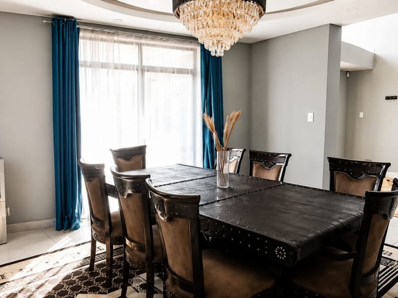 Spacious dining room featuring a recessed ceiling with a crystal chandelier, tiled flooring, and large sliding glass doors providing natural light.