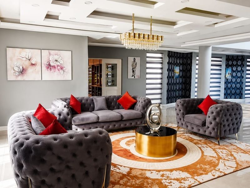 A spacious, modern living room featuring a sophisticated coffered ceiling with recessed lighting, a crystal chandelier, and polished tiled flooring.