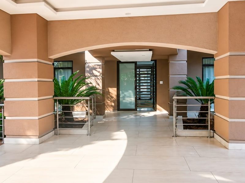 A grand, covered entrance featuring arched masonry columns, sleek stainless steel balustrades, and a modern glass front door, leading into the residence.