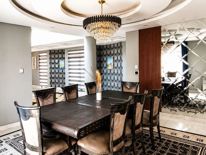 Elegant dining room featuring a recessed ceiling with a chandelier, decorative mirrored wall paneling, and sophisticated slatted wood accents.