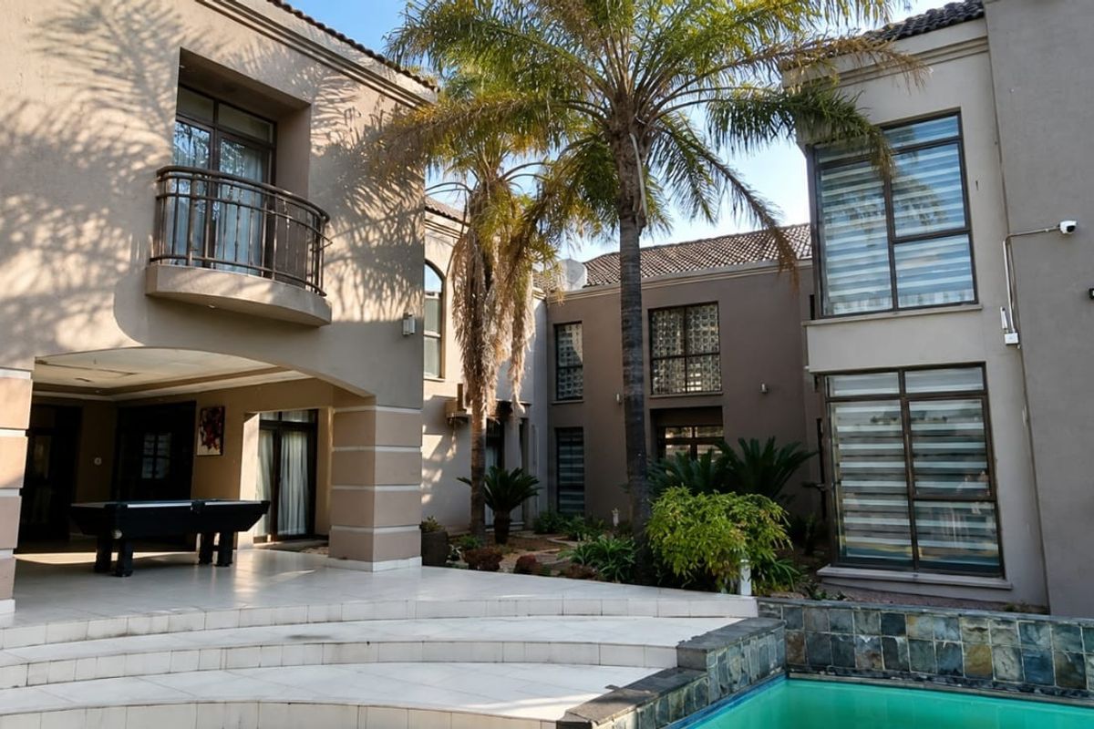 Rear exterior view featuring a tiled patio area, swimming pool, and a multi-story facade with a balcony and large windows.