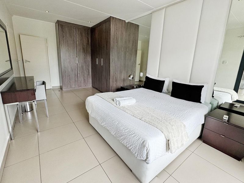 Spacious bedroom featuring large format floor tiles, built-in wooden cupboards, a mirrored feature wall, and integrated air conditioning.