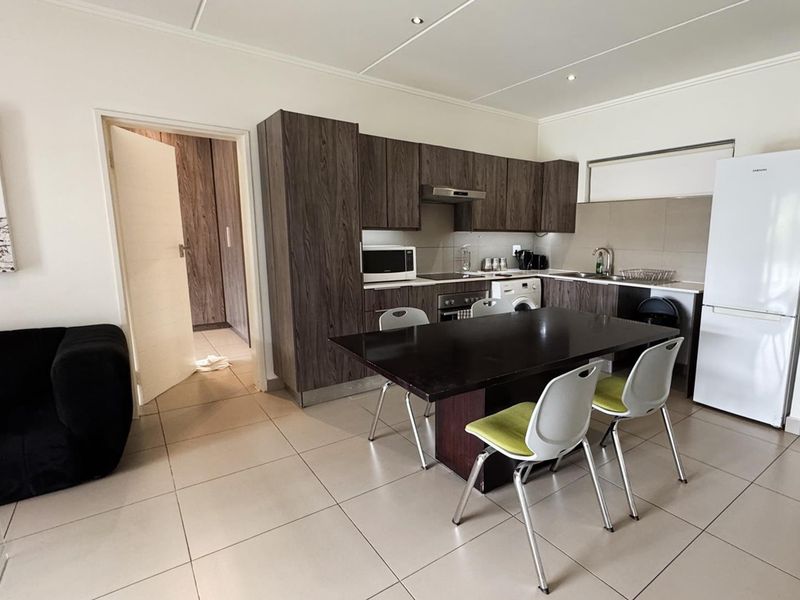 Open-plan kitchen and dining area featuring modern wood-grain cabinetry, tiled flooring, and integrated appliances, creating a functional and cohesive living space.