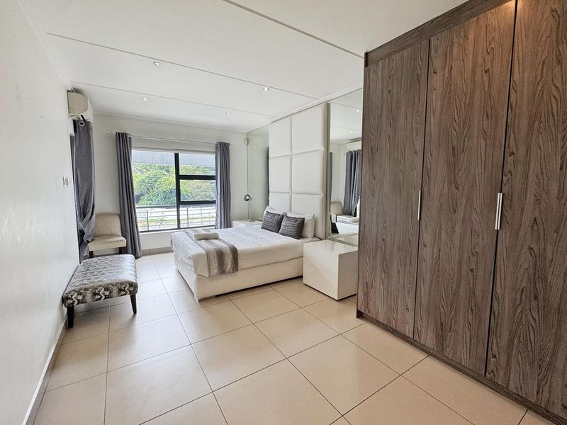 Spacious bedroom featuring large built-in wardrobes, tiled flooring, recessed lighting, and a modern upholstered headboard wall panel with integrated mirrors.