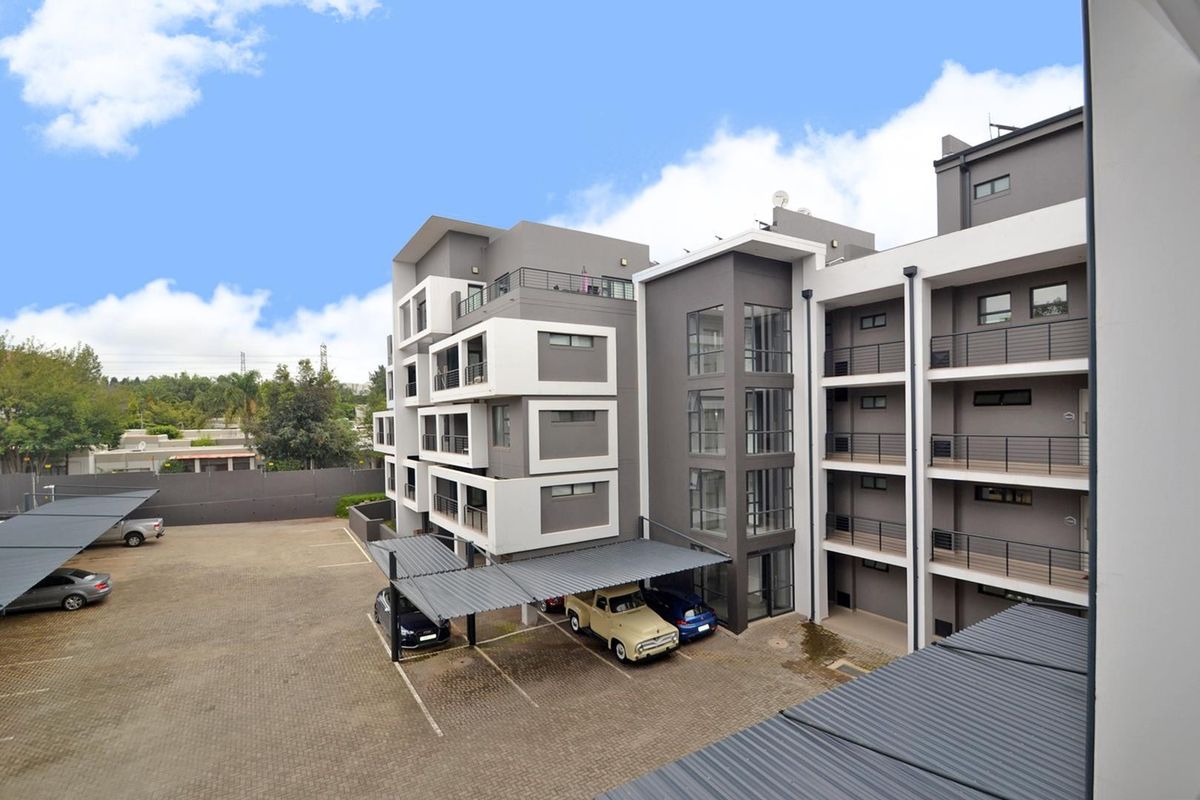 Exterior view of a modern apartment complex featuring paved parking, covered parking bays, and multi-level balconies with contemporary architectural finishes.