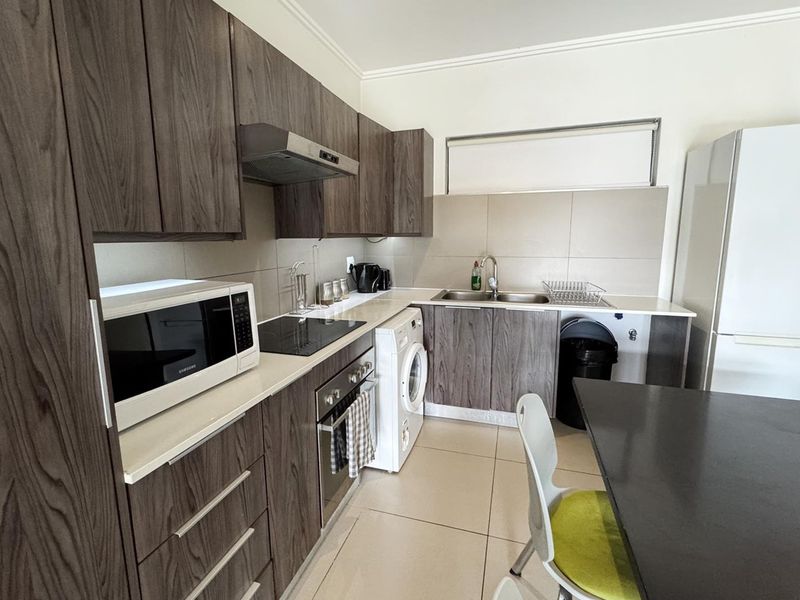 A functional kitchen featuring wood-grain cabinetry, stone-look countertops, integrated appliances, and neutral tiled flooring, offering a clean and practical workspace.