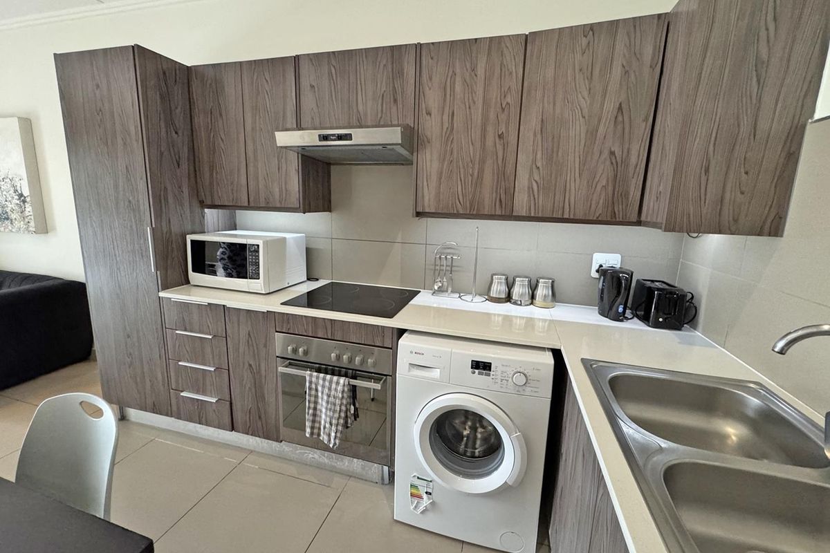 Modern kitchen featuring wood-grain cabinetry, stone countertops, integrated appliances including a washing machine, and a sleek tiled backsplash.