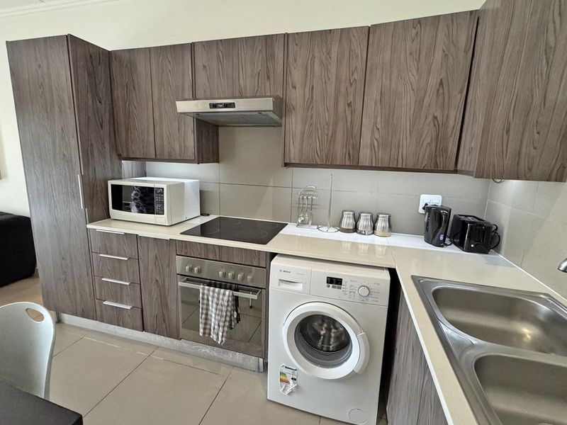Modern kitchen featuring wood-grain cabinetry, stone countertops, integrated appliances including a washing machine, and a sleek tiled backsplash.