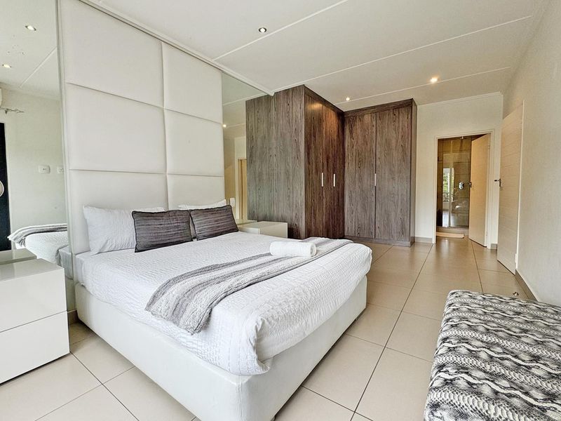 Spacious bedroom featuring modern tiled flooring, extensive built-in wooden cupboards, and a stylish upholstered headboard wall with integrated mirrored panels.