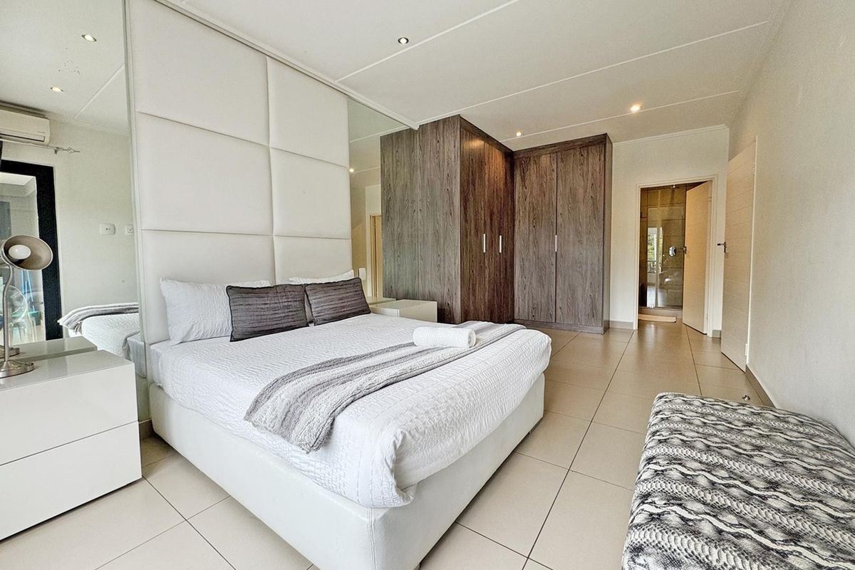 Spacious bedroom featuring modern tiled flooring, extensive built-in wooden cupboards, and a stylish upholstered headboard wall with integrated mirrored panels.