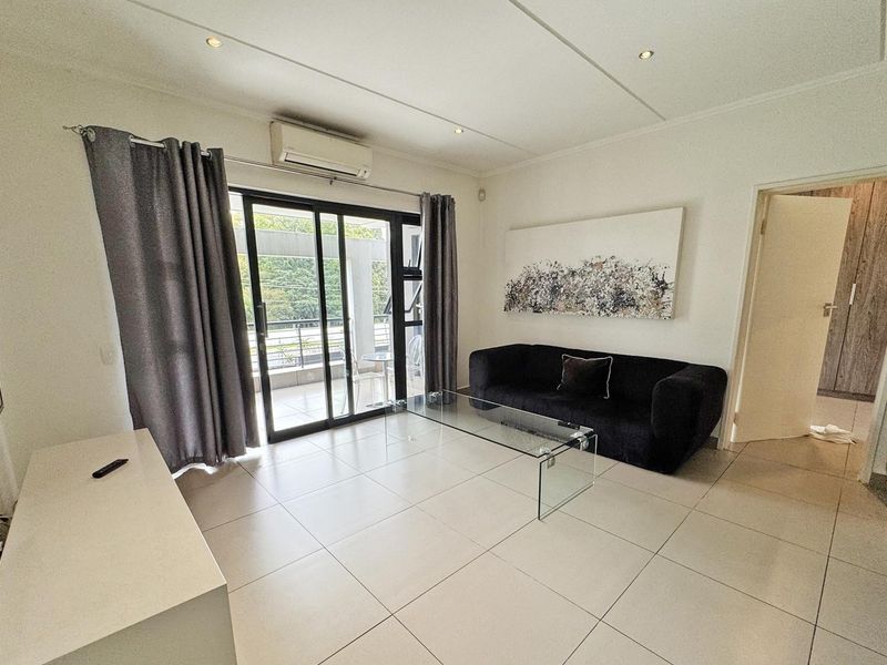 A bright living room featuring tiled flooring, recessed lighting, a wall-mounted air conditioner, and sliding glass doors providing access to the balcony.