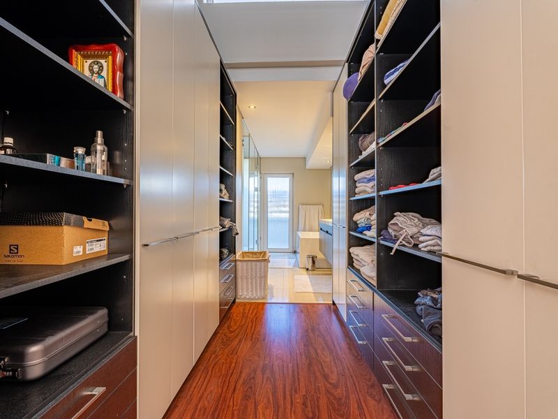 A well-organized walk-in wardrobe featuring extensive built-in cabinetry, shelving, and warm hardwood flooring, leading directly into an adjoining bathroom.