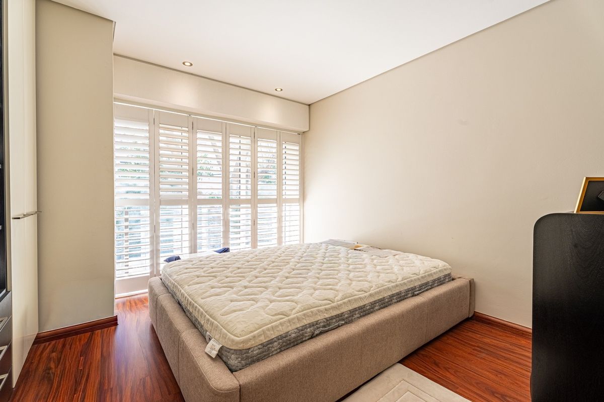 A well-maintained bedroom featuring warm laminate flooring, recessed downlighting, and white plantation shutters providing natural light control.
