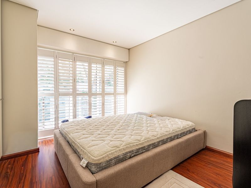 A well-maintained bedroom featuring warm laminate flooring, recessed downlighting, and white plantation shutters providing natural light control.