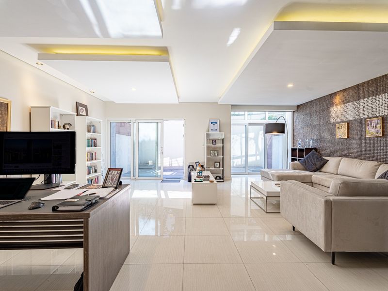 Spacious open-plan living area featuring high-gloss tiled floors, a modern coffered ceiling with recessed lighting, and large sliding glass doors leading to the exterior.