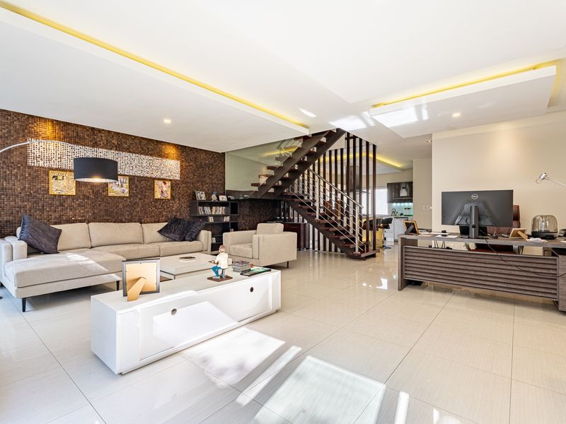 Spacious open-plan living area featuring a modern staircase with glass balustrade, tiled flooring, and a decorative feature wall with recessed ceiling lighting.